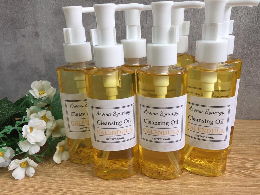 Bottles of golden calendula cleansing oil with white pump tops and dried petals inside