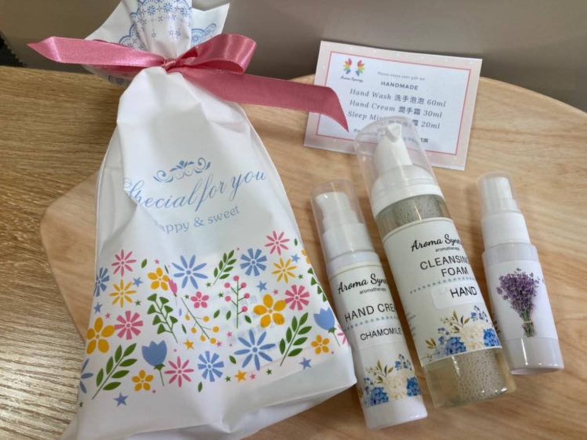 Aroma Synergy gift pouch made from reusable printed fabric, shown with hand cream, cleansing foam and a lavender sleep mist
